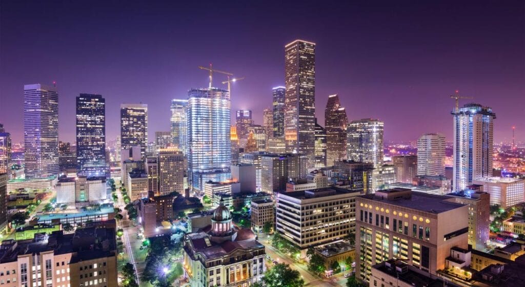 A city skyline at night with illuminated high-rise buildings, construction cranes, and a historic building in the foreground—perfect for a memorable Sightseeing Tour.